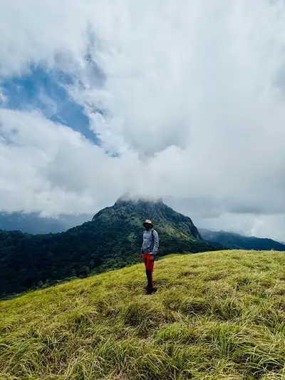 Trekker on a grassy ridge below a cloud-capped peak, Silent Valley trek