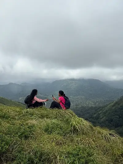 Two trekkers resting on a grassy slope above misty valleys in Silent Valley